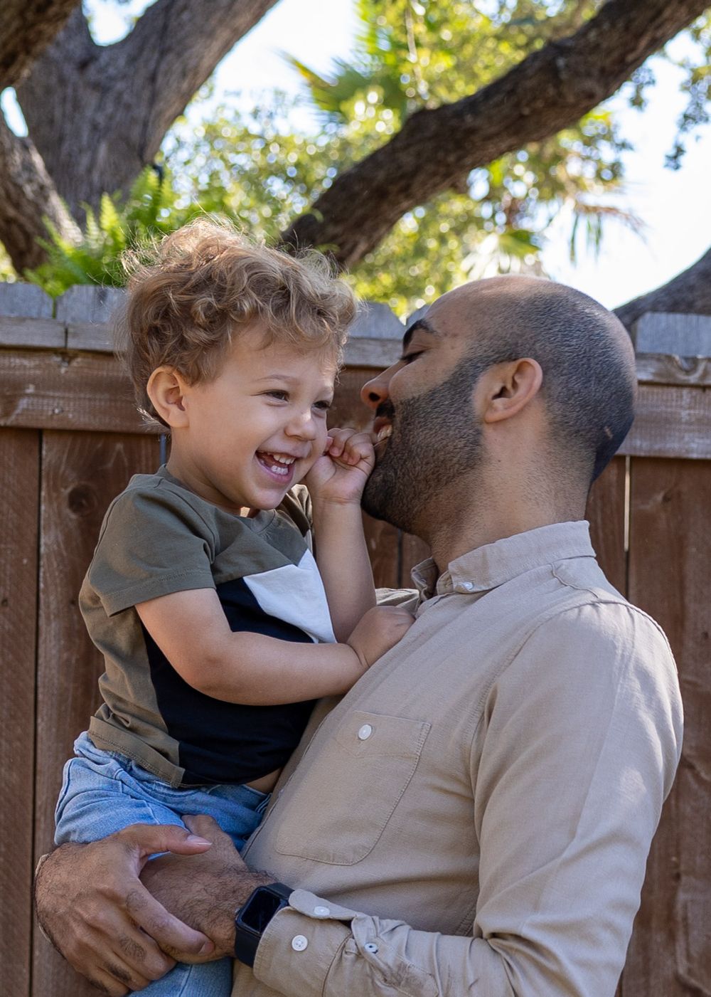 Joyful moment shared between parent and young child outdoors with wooden fence in background.