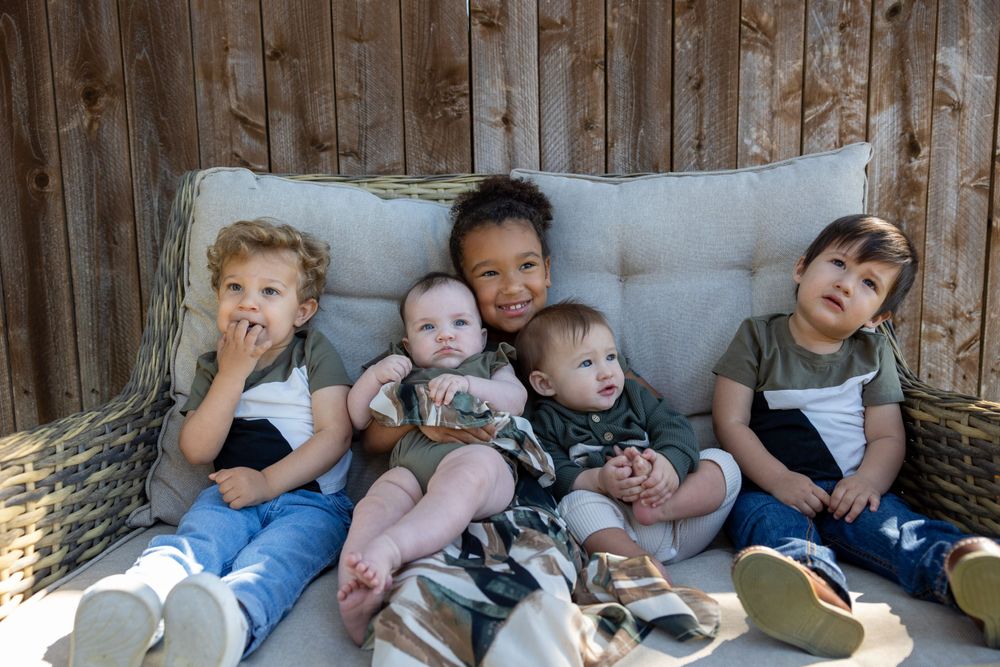 Group of children sitting together on outdoor cushioned bench.