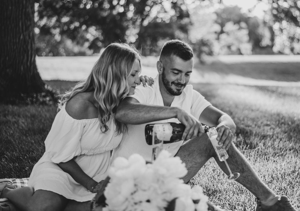 Couple enjoying romantic picnic on grass with wine and laughter.