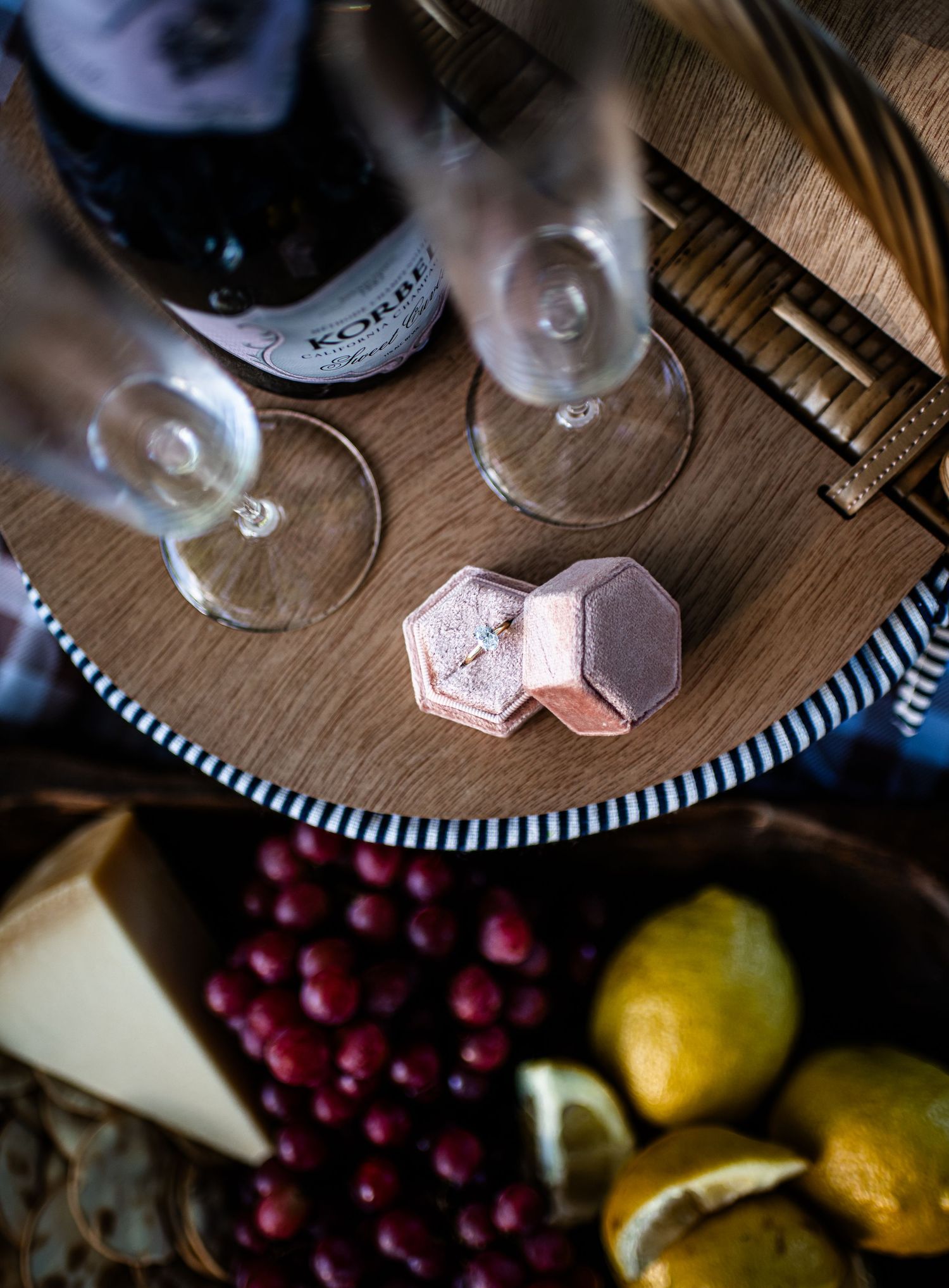 Still life of wine glasses and fruit on wooden surface with dramatic lighting.