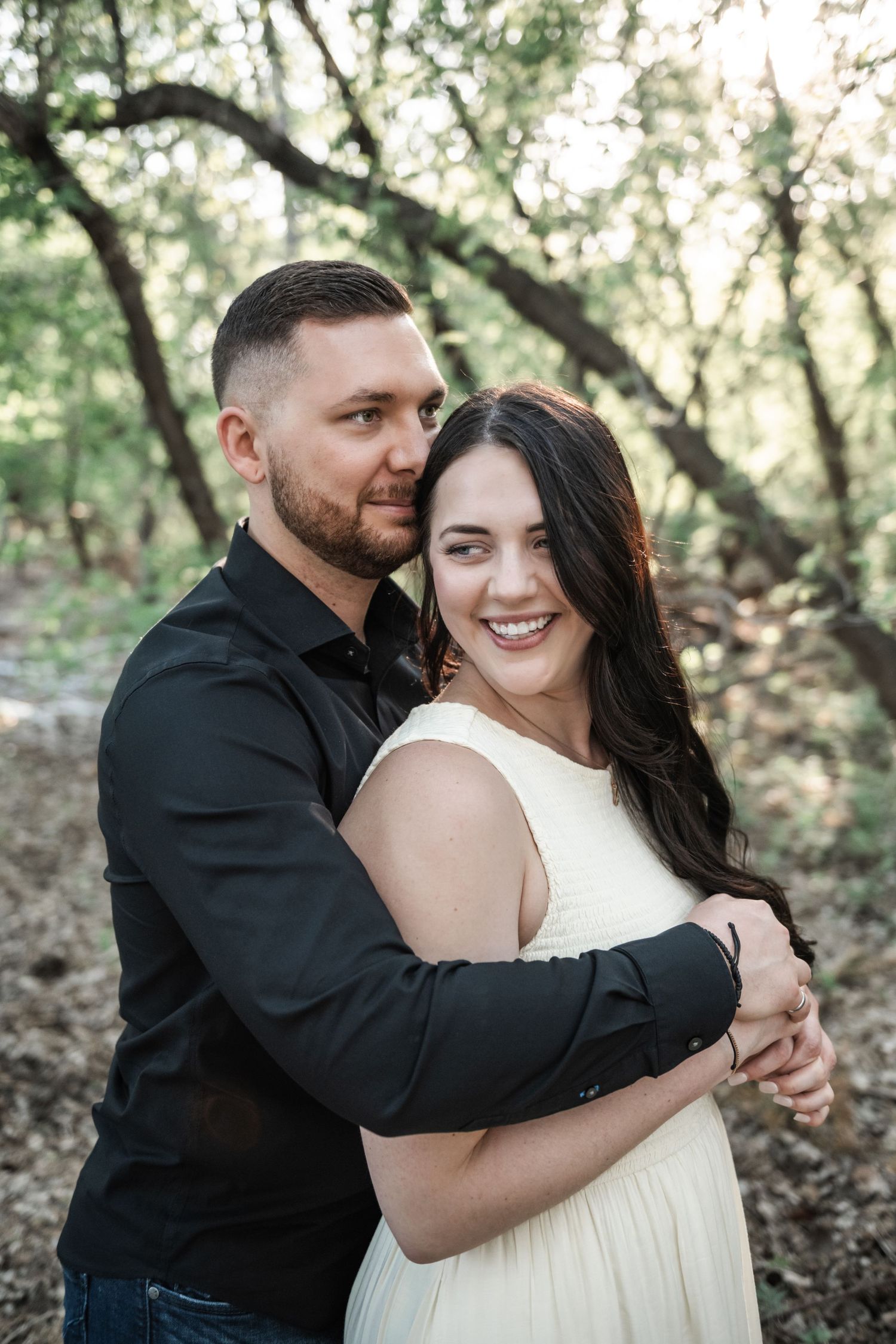 A couple embraces in a romantic portrait among trees during golden hour.