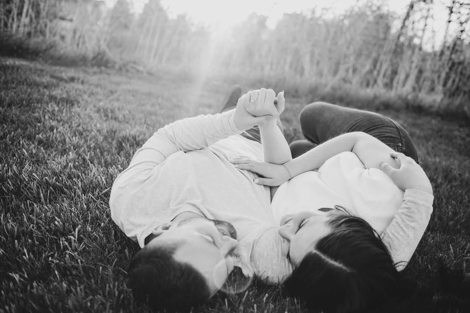 Couple in white outfits lying together on grass during an outdoor photo session.
