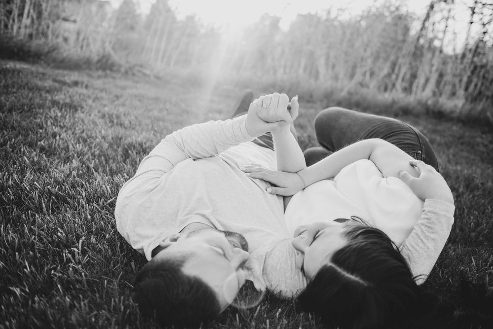 Couple in white outfits lying together on grass during an outdoor photo session.