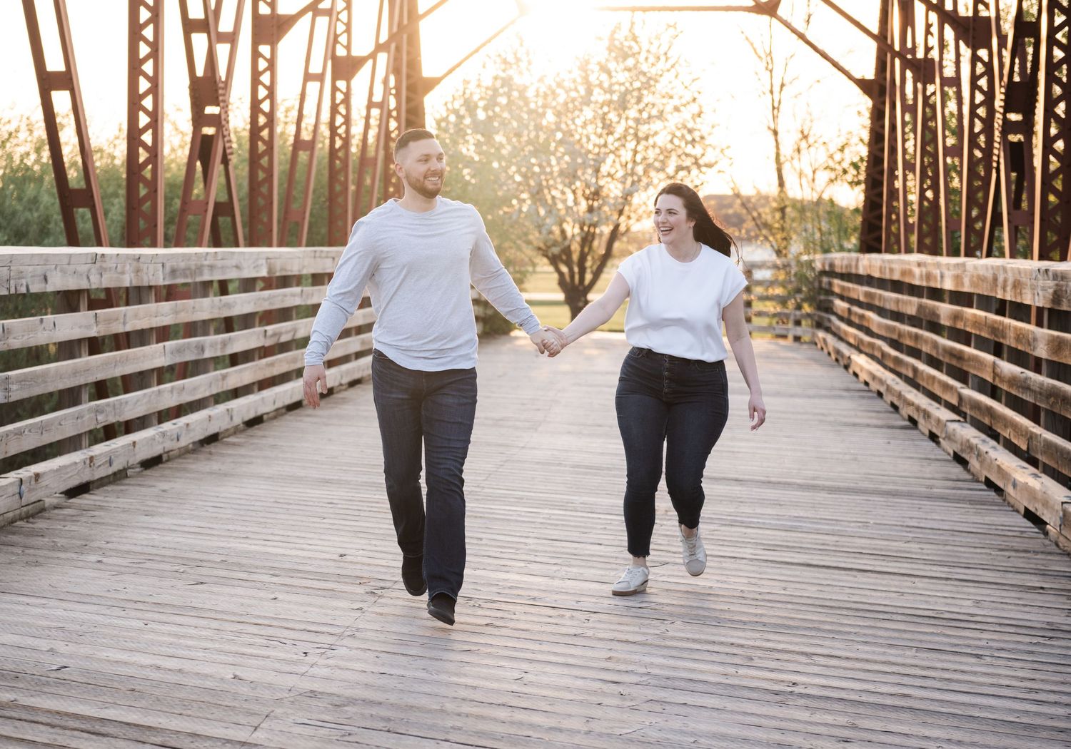 Couple walking hand in hand across a wooden bridge during golden hour.