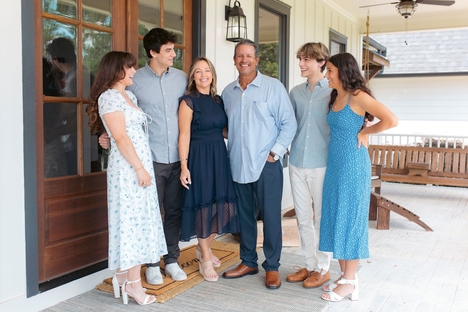 A group gathers on a front porch for a casual outdoor portrait on a sunny day.