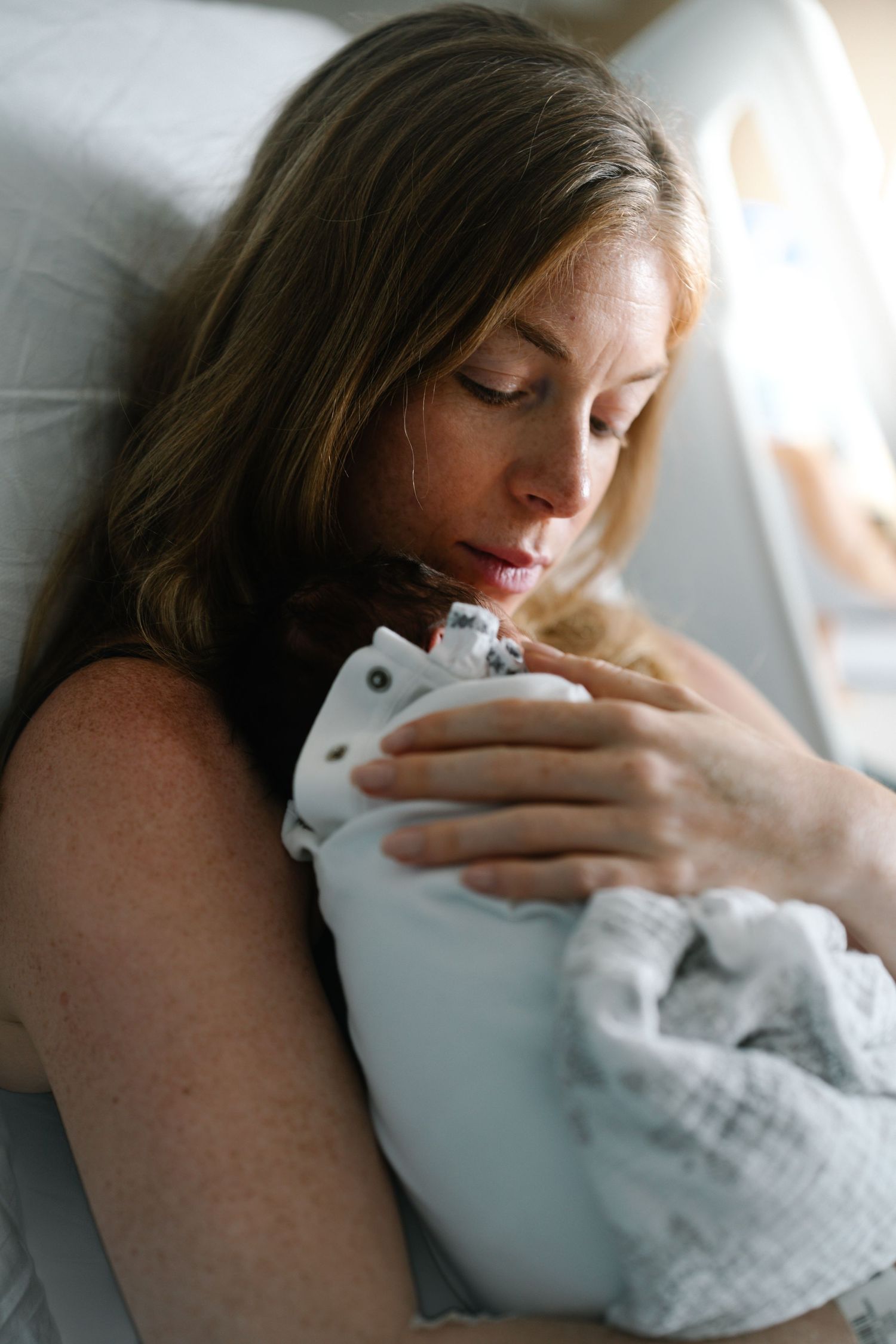 Mother tenderly cuddles newborn baby wrapped in white blanket.