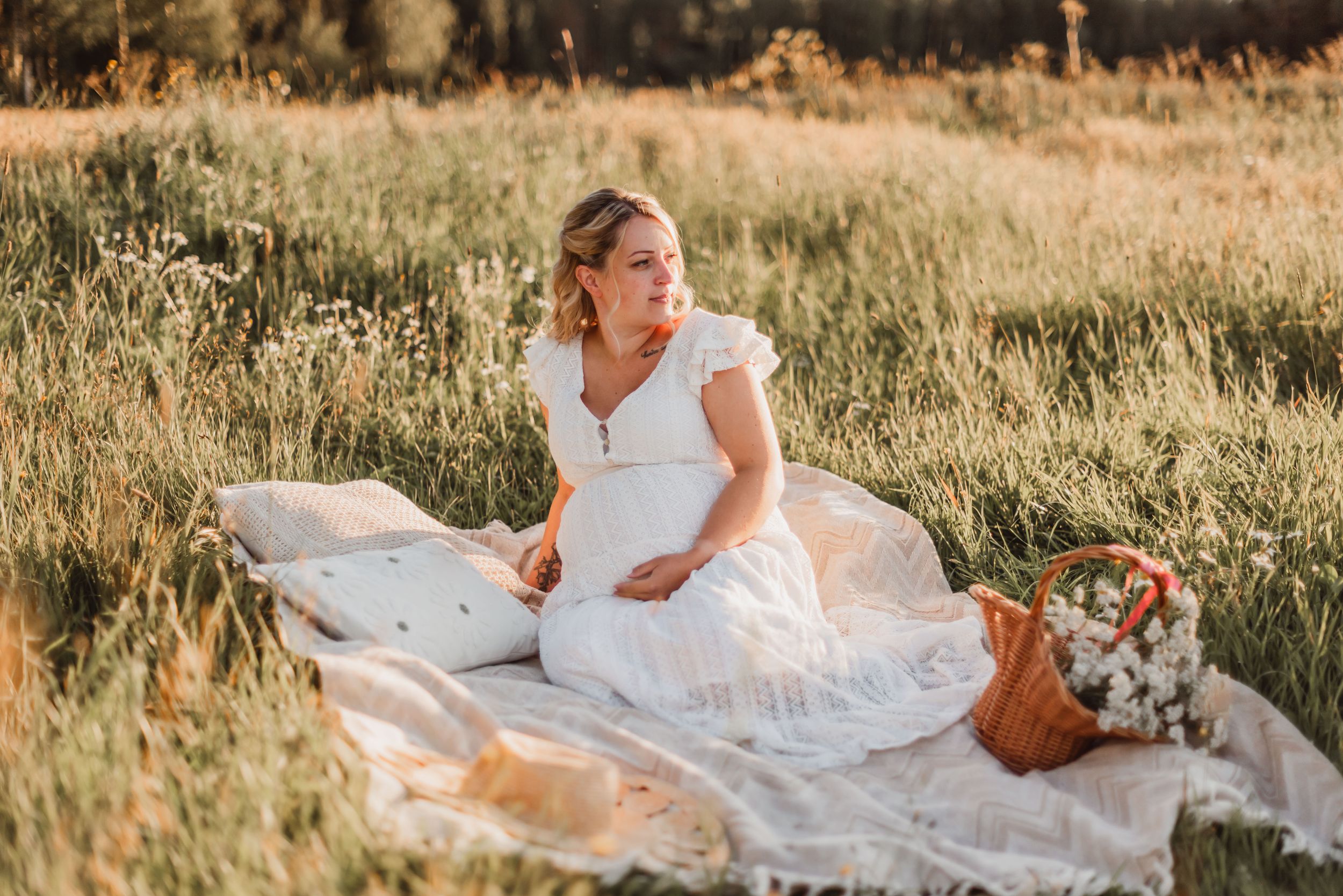 A person in a white wedding dress lies gracefully in a sunlit meadow during golden hour.