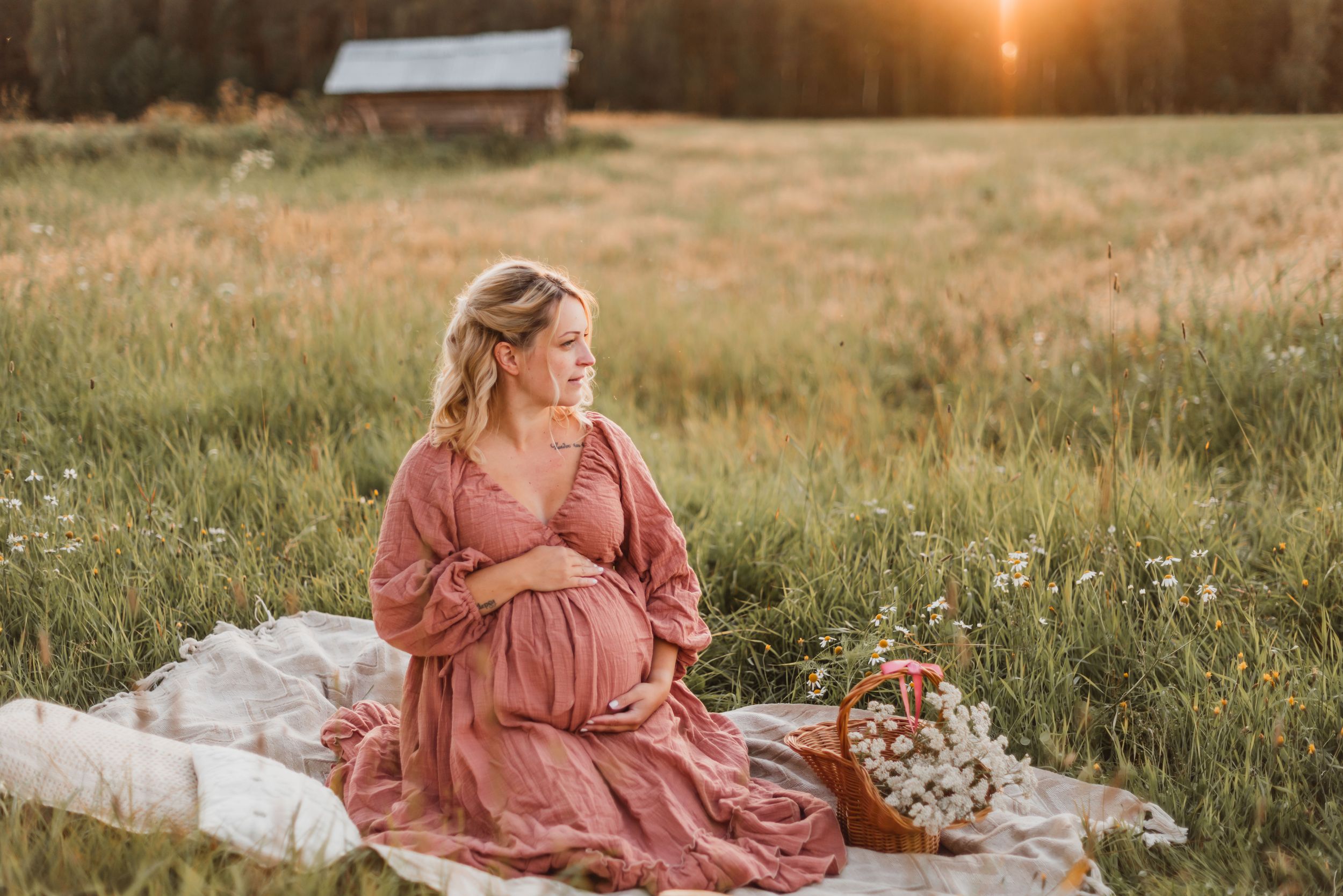 A person in a flowing pink dress sits in a golden meadow at sunset, creating a dreamy ethereal scene.