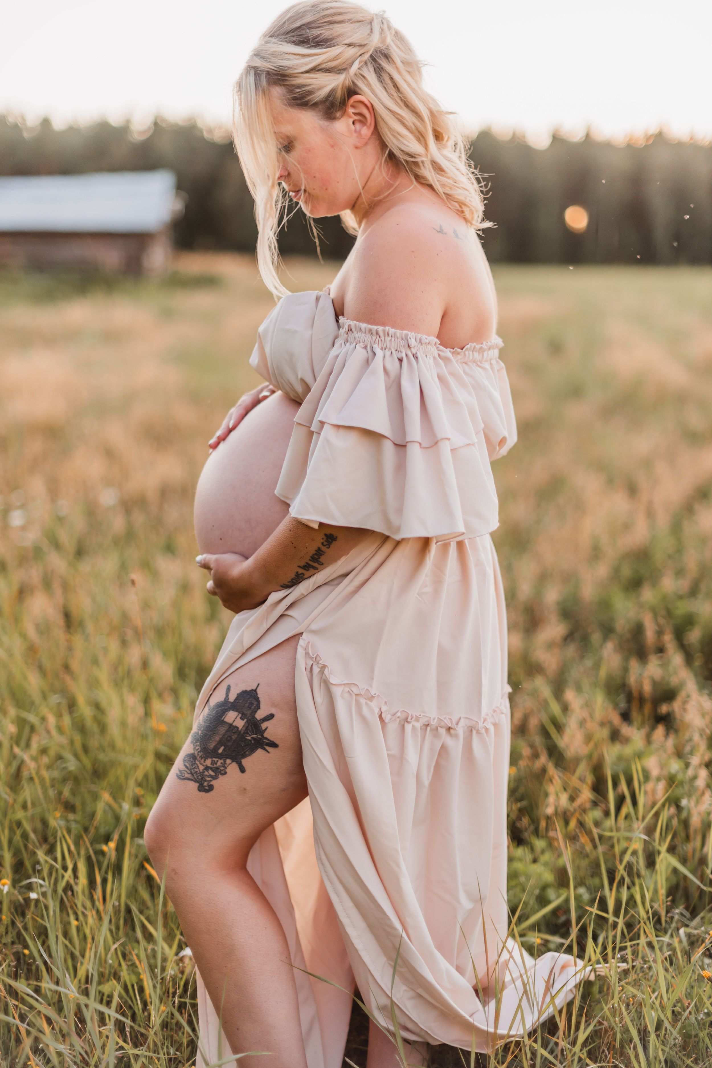 Ethereal maternity photoshoot in a golden field at sunset shows woman in flowy off-shoulder dress.