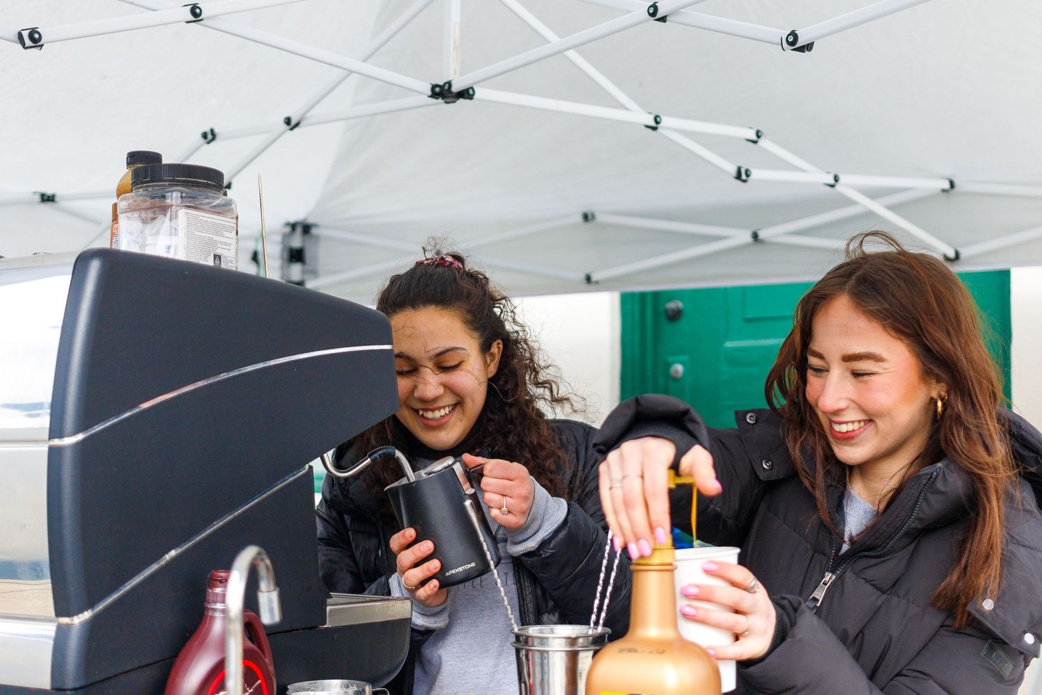 Two friends enjoying drinks at an outdoor market vendor booth.
