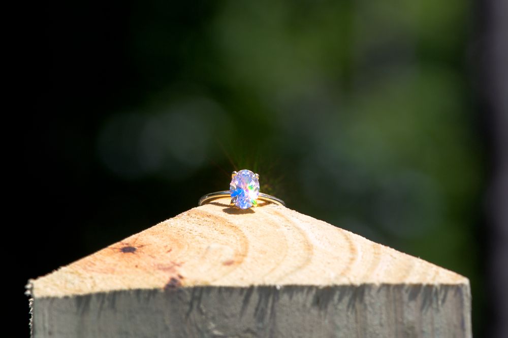 A delicate sapphire engagement ring perched on wooden surface in natural lighting.
