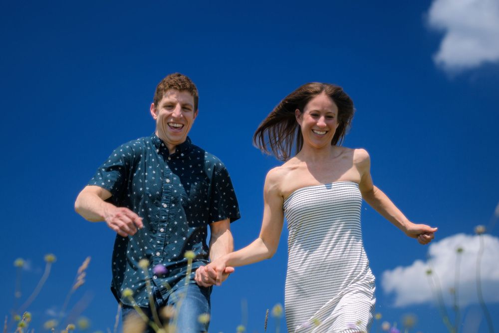 A couple running through a summer meadow against bright blue sky.