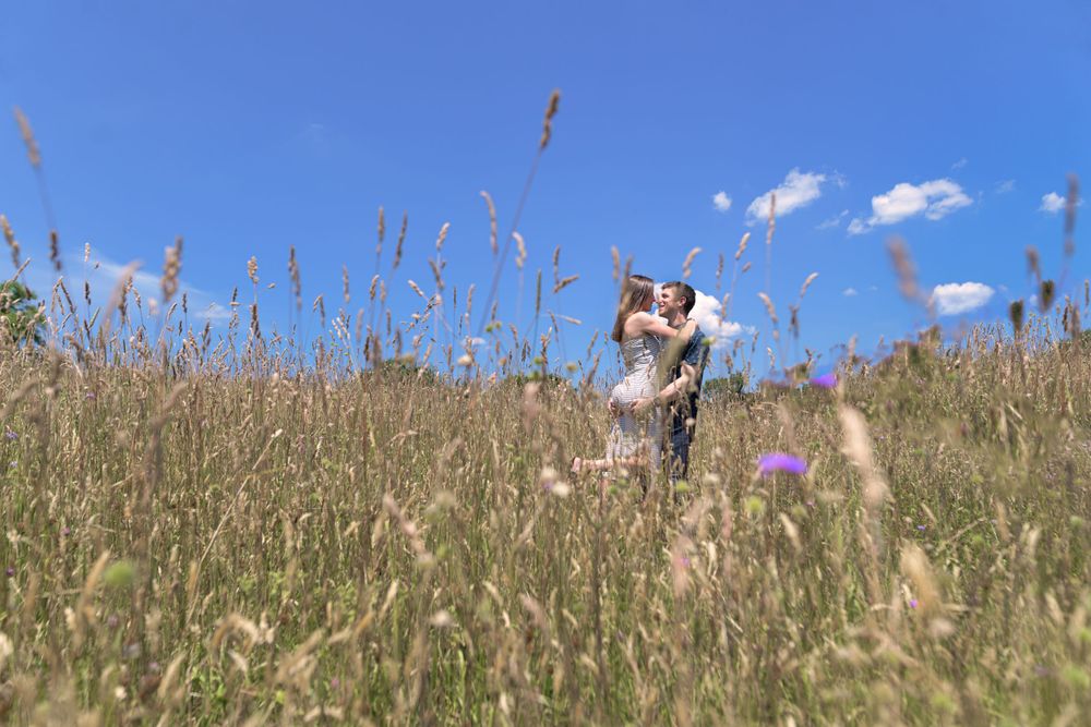 Two people embracing in a tall grass field against a bright blue summer sky.
