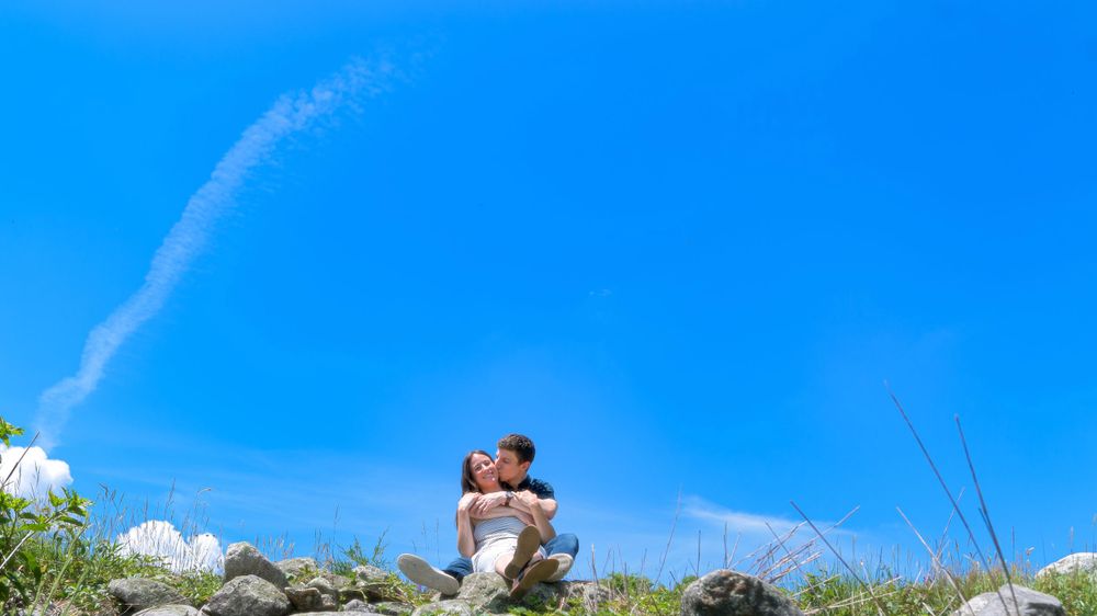 A romantic moment captured on a hilltop against a vivid blue sky.