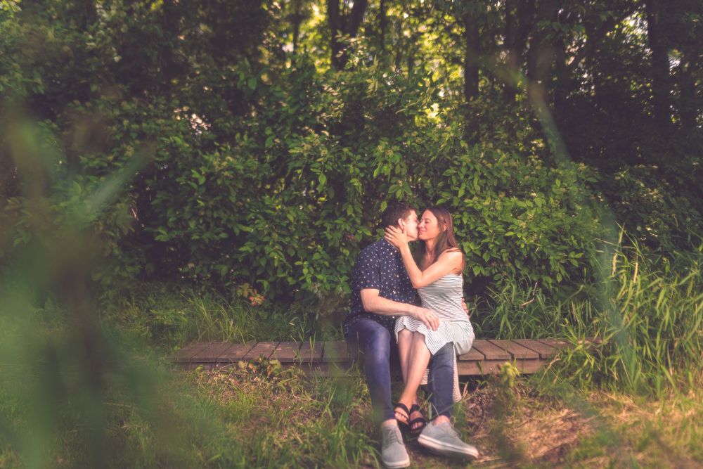 A couple sitting close together on a wooden bench surrounded by lush green foliage.