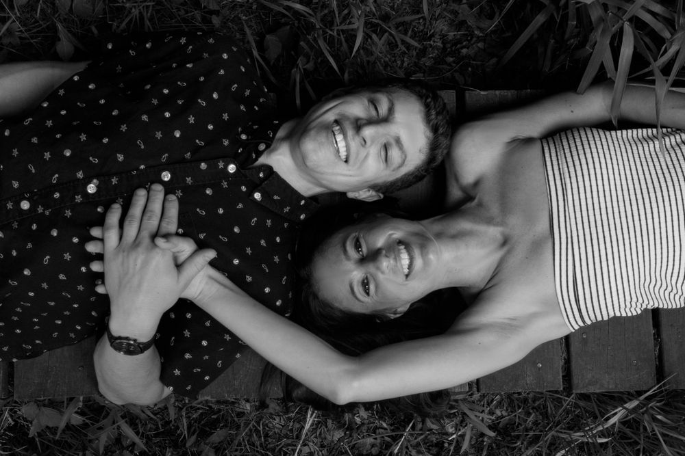 A black and white photo showing two people lying in grass and laughing together.