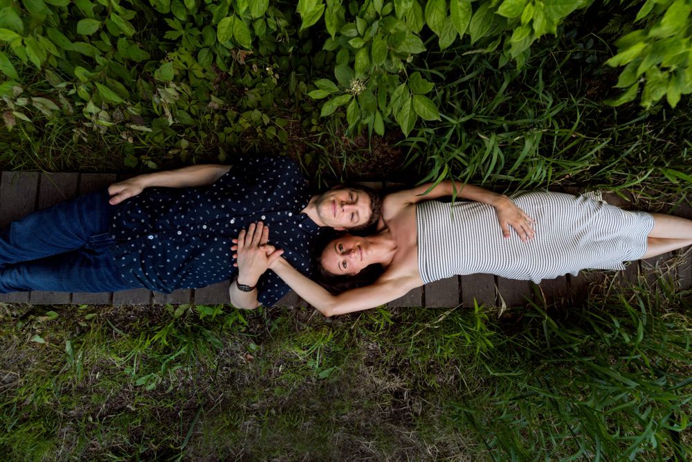 Two people lying on grass together surrounded by lush green foliage.
