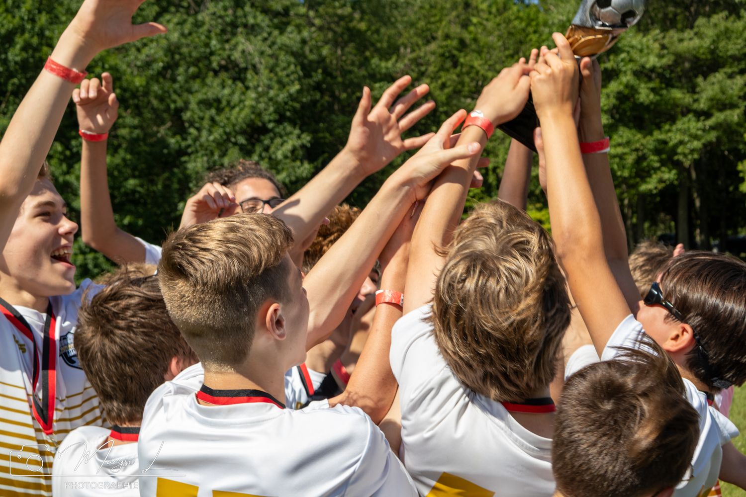 Sports team celebrating victory by raising trophy together outdoors.