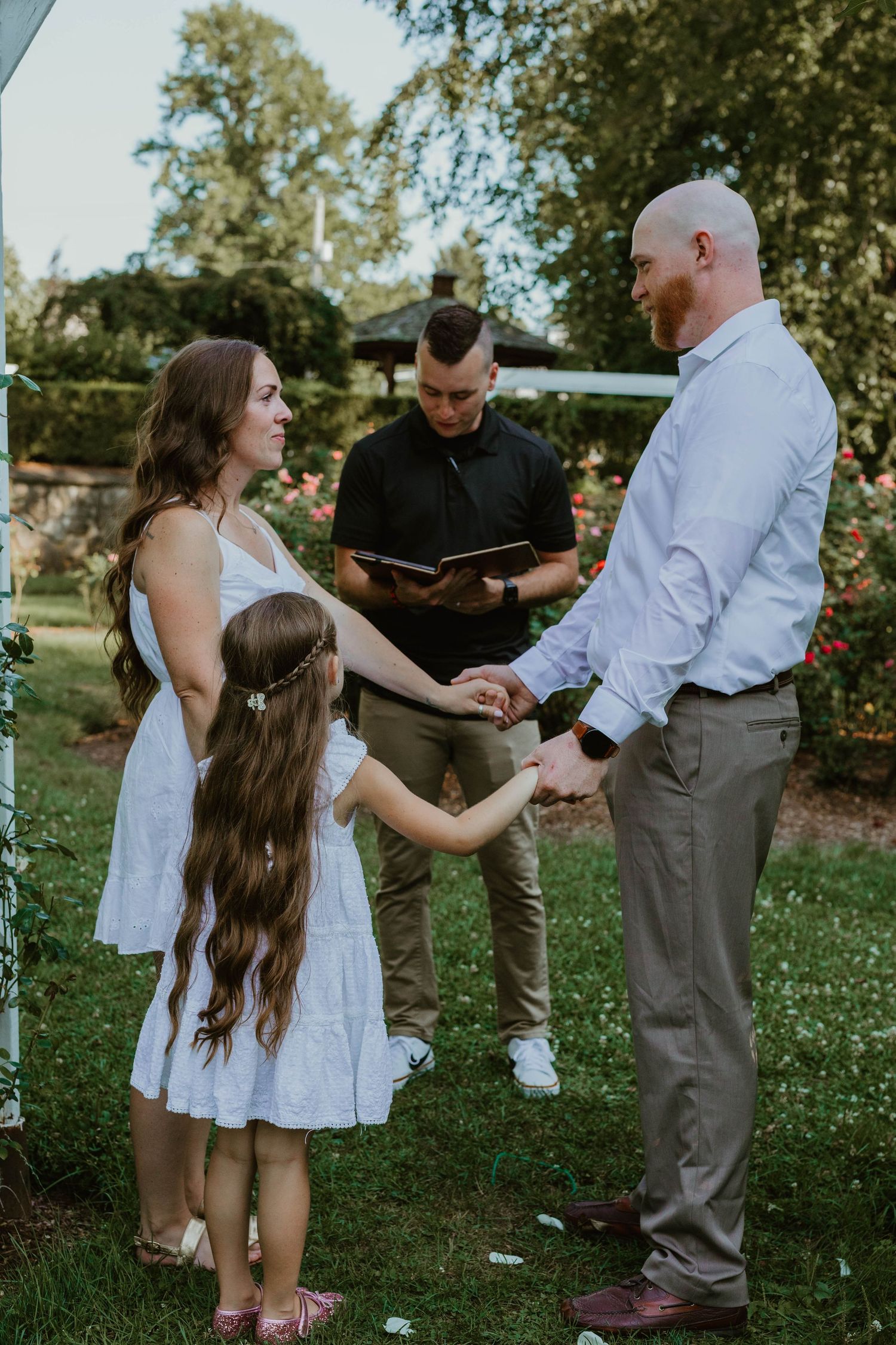 Family interacts playfully in outdoor garden setting during summer photo session.