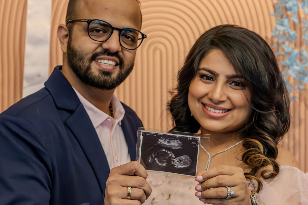 Couple holding ultrasound photo against geometric orange background.