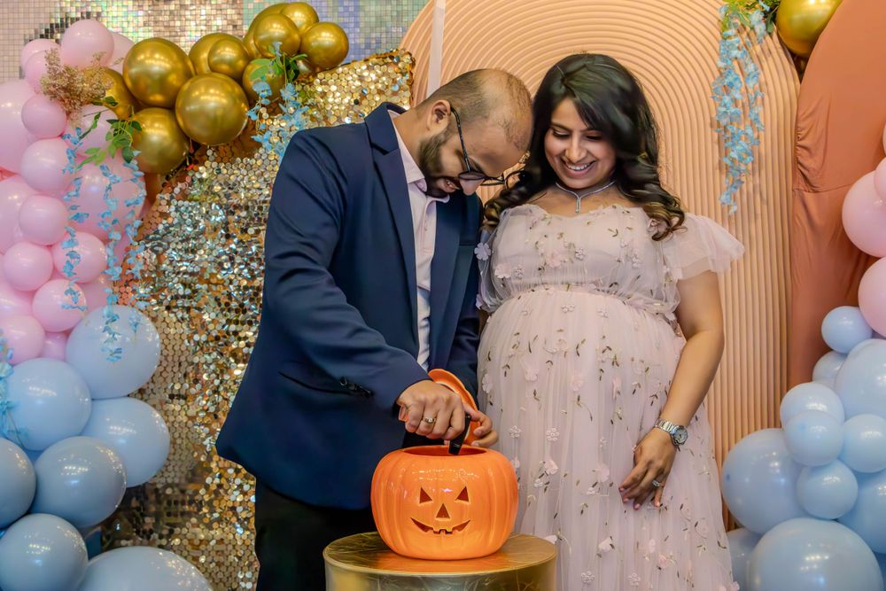 Couple carving a pumpkin at gender reveal party with pink and gold balloon decorations.