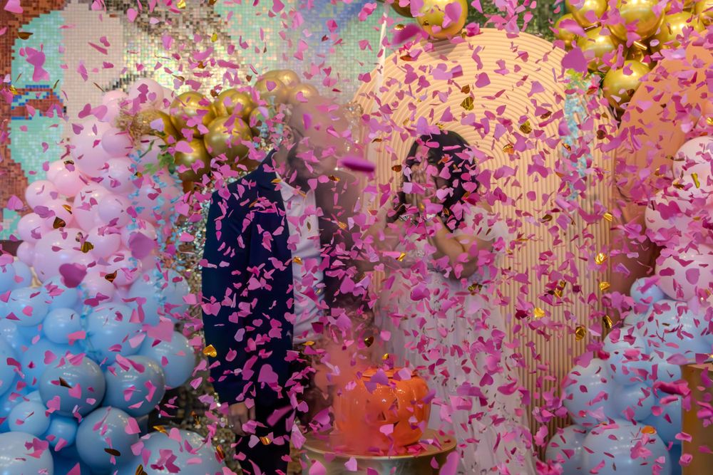 Explosion of pink and gold confetti against colorful balloon backdrop at celebration.