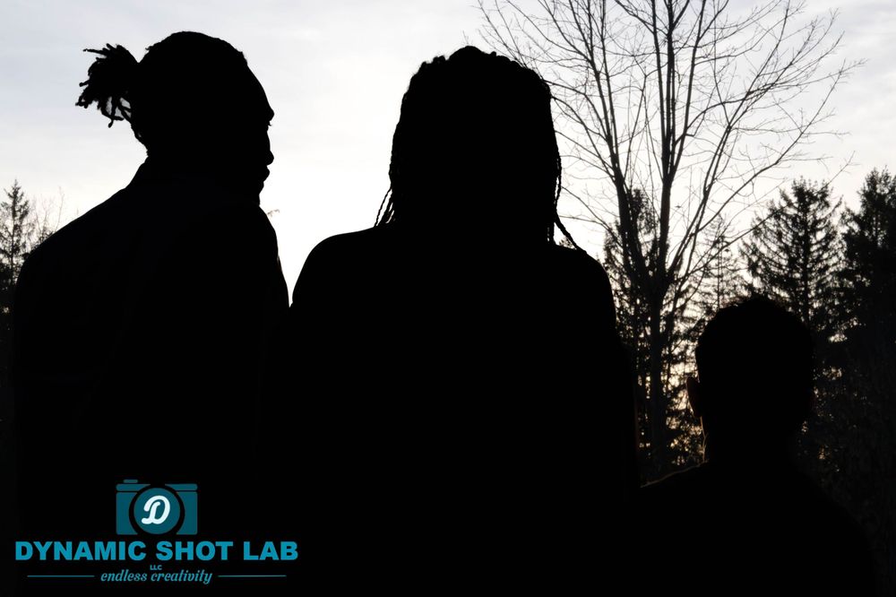 Silhouettes of three people against a sunset sky with bare trees in the background.