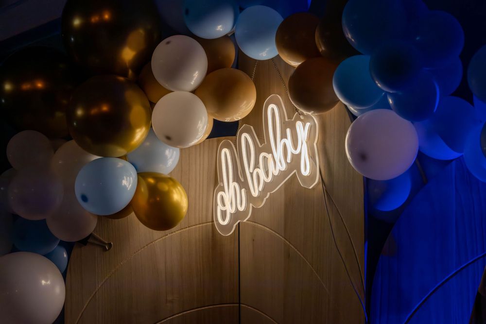 Illuminated 'Oh Baby' neon sign surrounded by blue and gold balloon decorations.