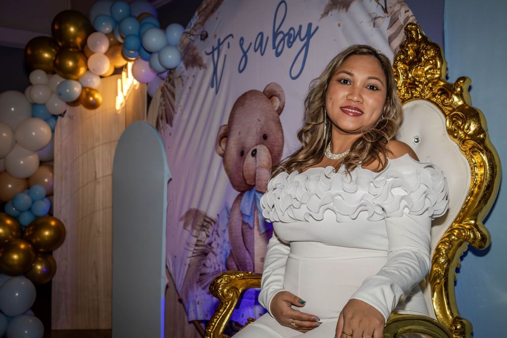 A baby shower celebration with white and gold balloon decorations and a decorative throne chair.