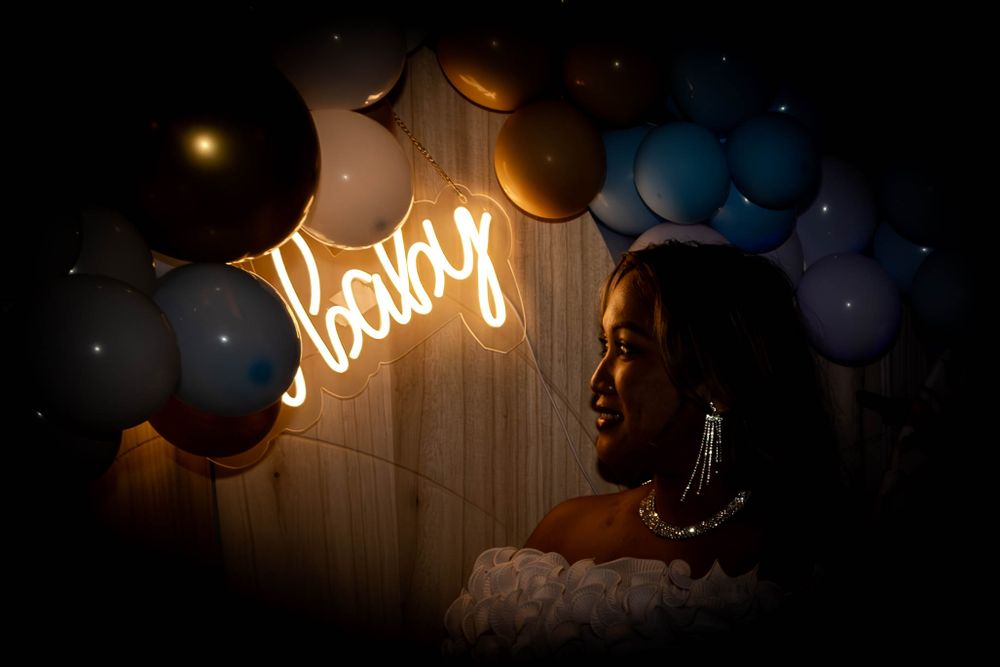 A silhouette against a neon 'baby' sign with blue and gold balloons.