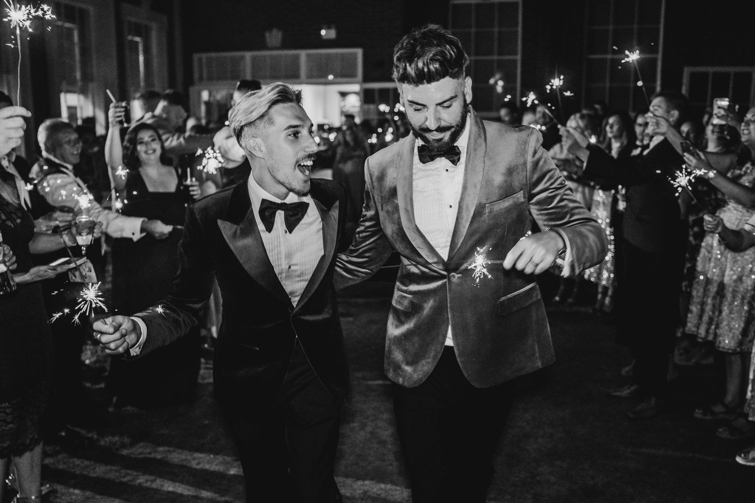 Joyful celebration with sparklers during an evening wedding reception in black and white.