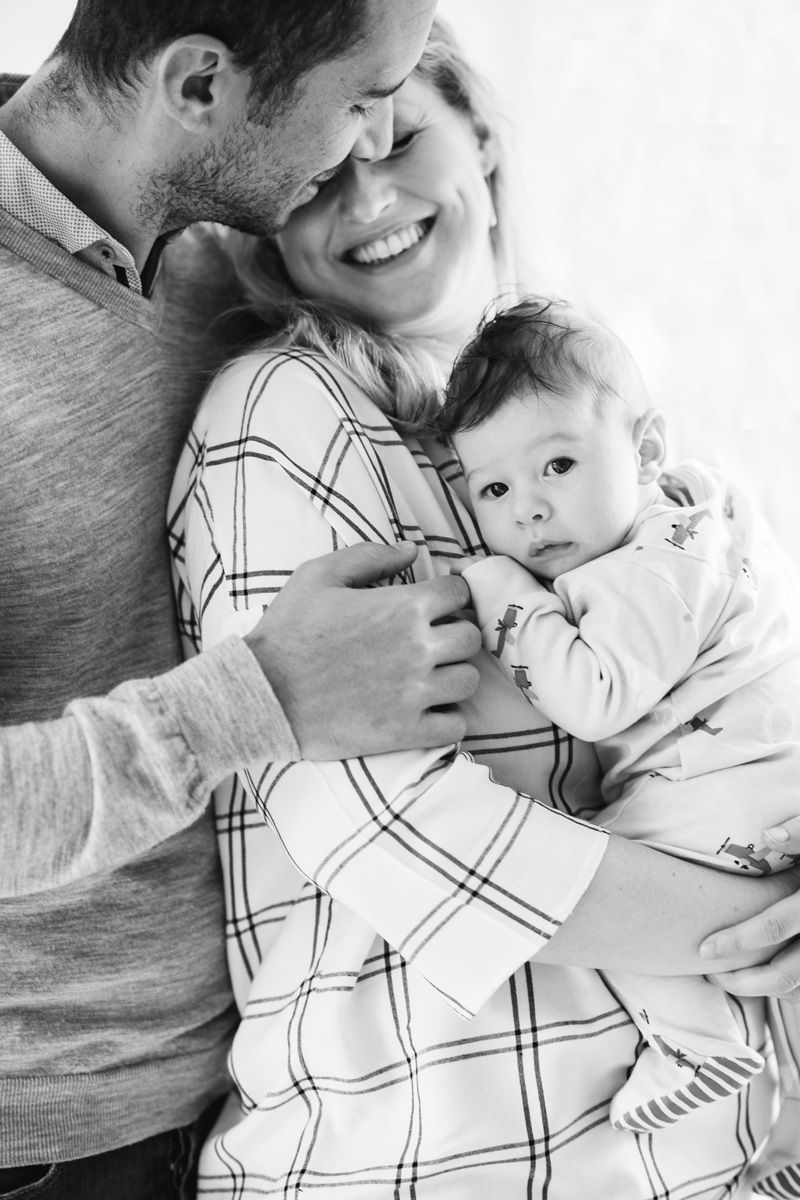 Black and white photo of parents smiling and holding their newborn, showcasing intimate family photography.