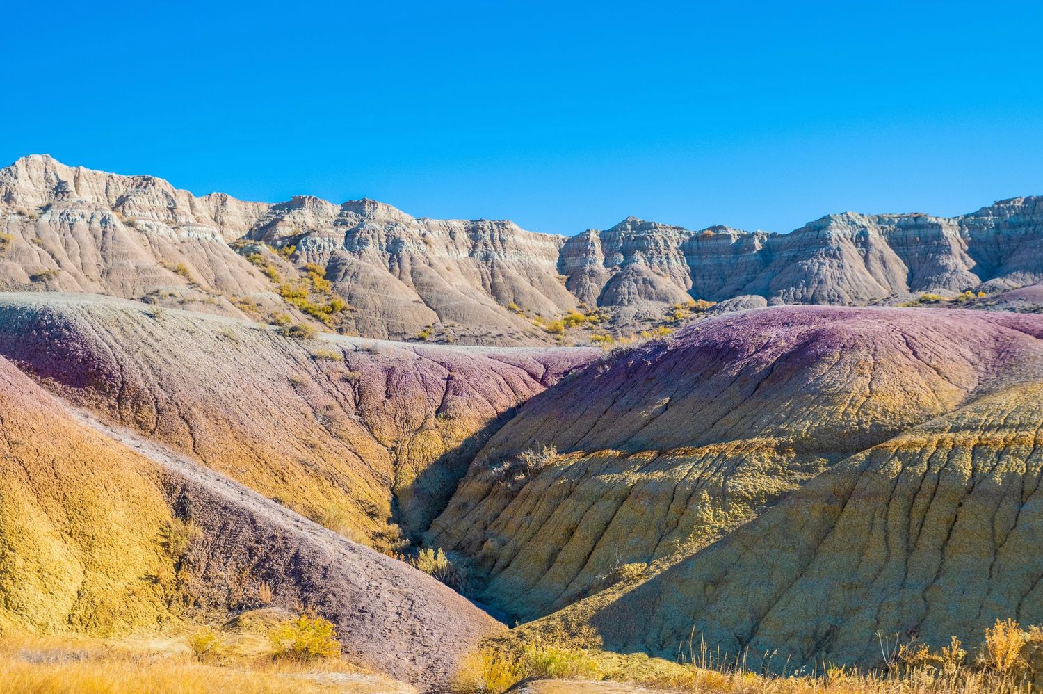 Multicolored badlands formations create dramatic landscape under vivid blue sky.