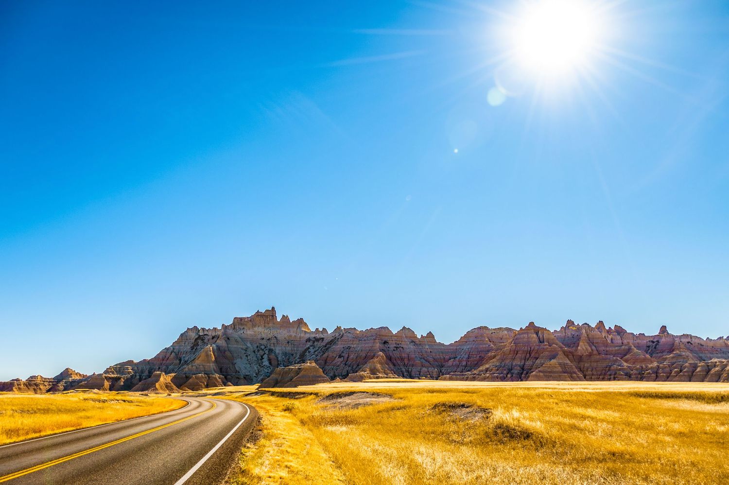 Scenic road leading through golden grasslands towards rugged mountain formations in Badlands National Park.