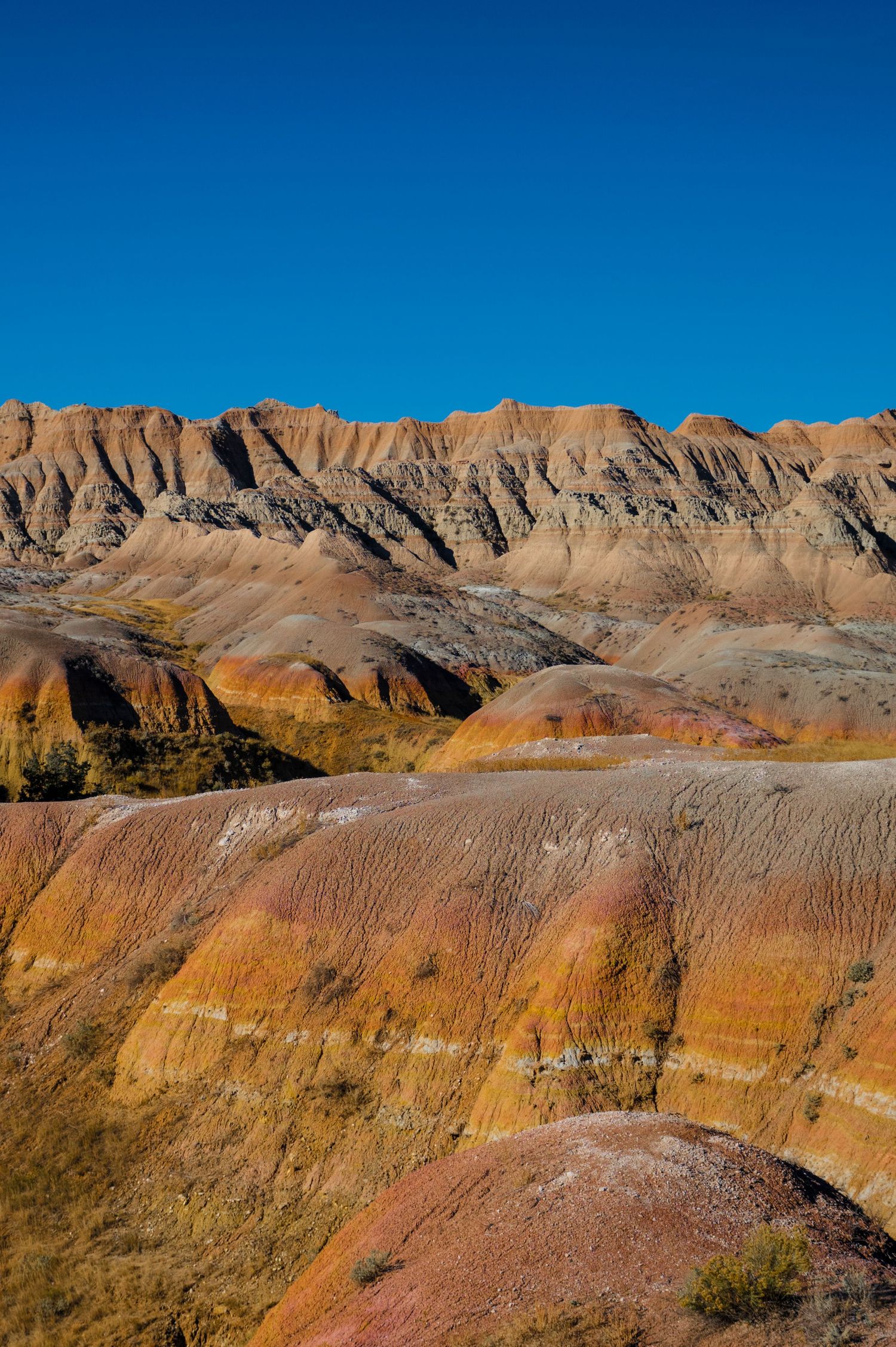 Colorful striped rock formations in Badlands National Park under bright blue sky.