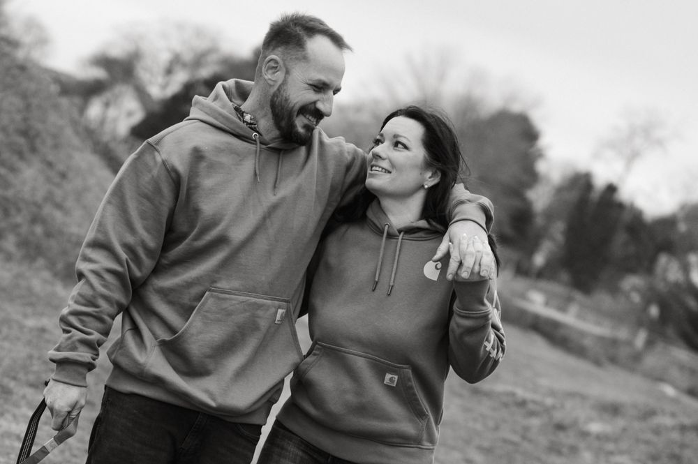 A couple in casual clothing share a loving moment while walking together outdoors on an overcast day.