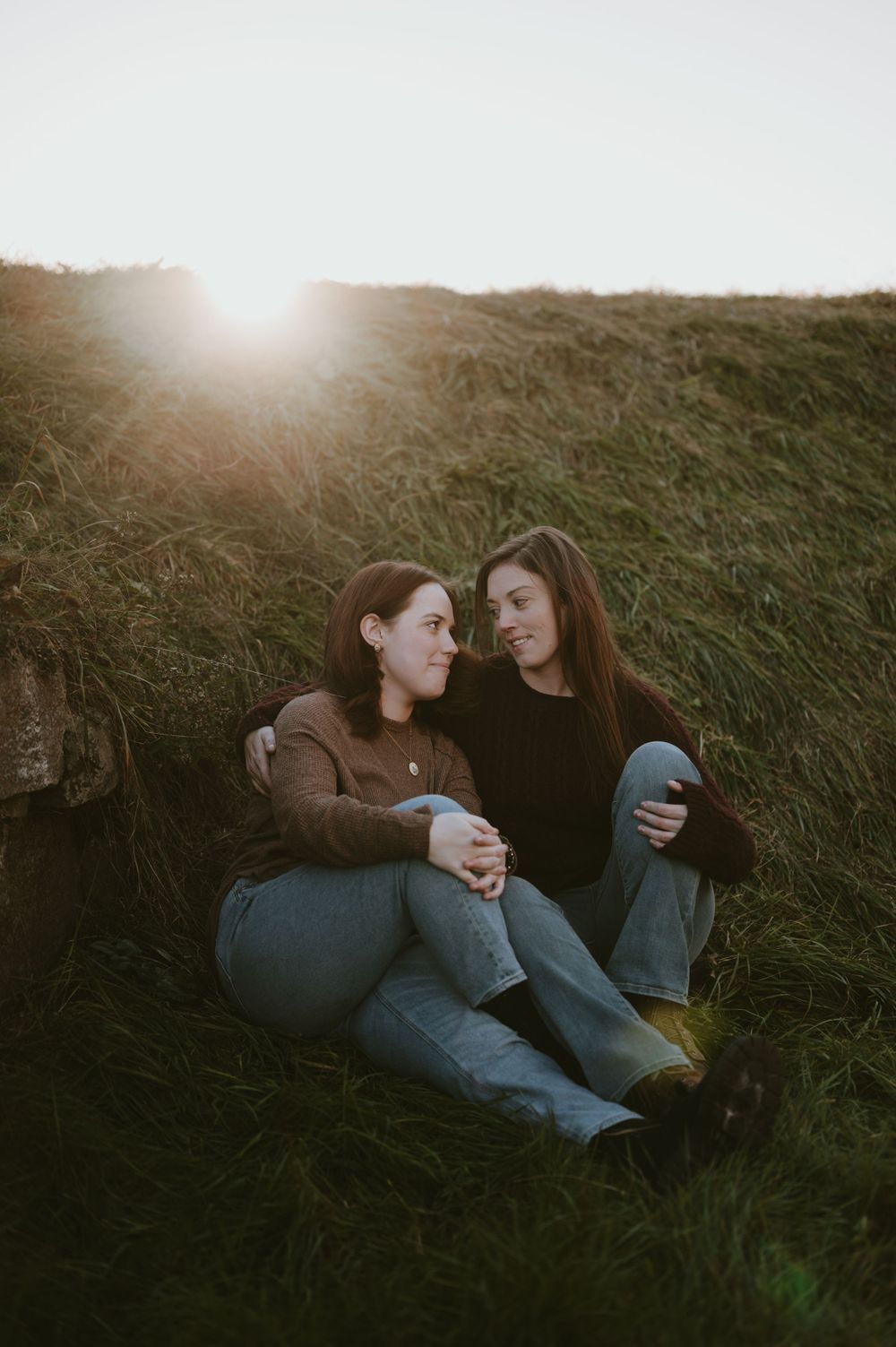 Two friends sitting together on grassy hillside at sunset.