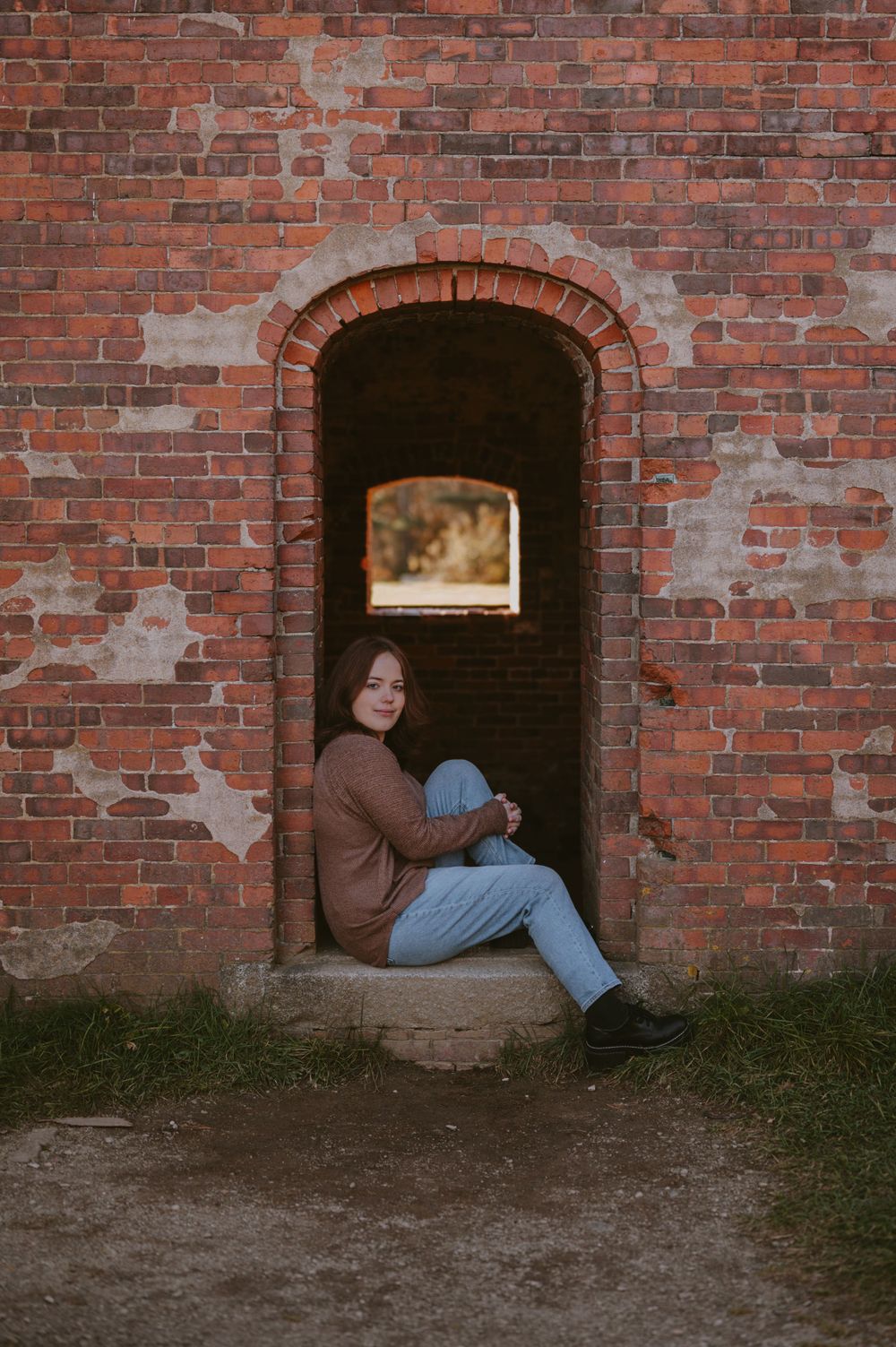 Person sitting in brick archway wearing casual clothes.