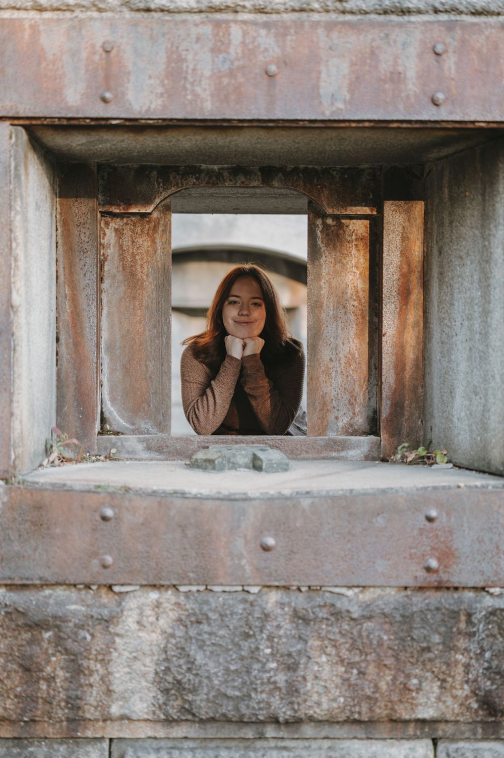 Person peering through square concrete opening with vintage weathered texture.