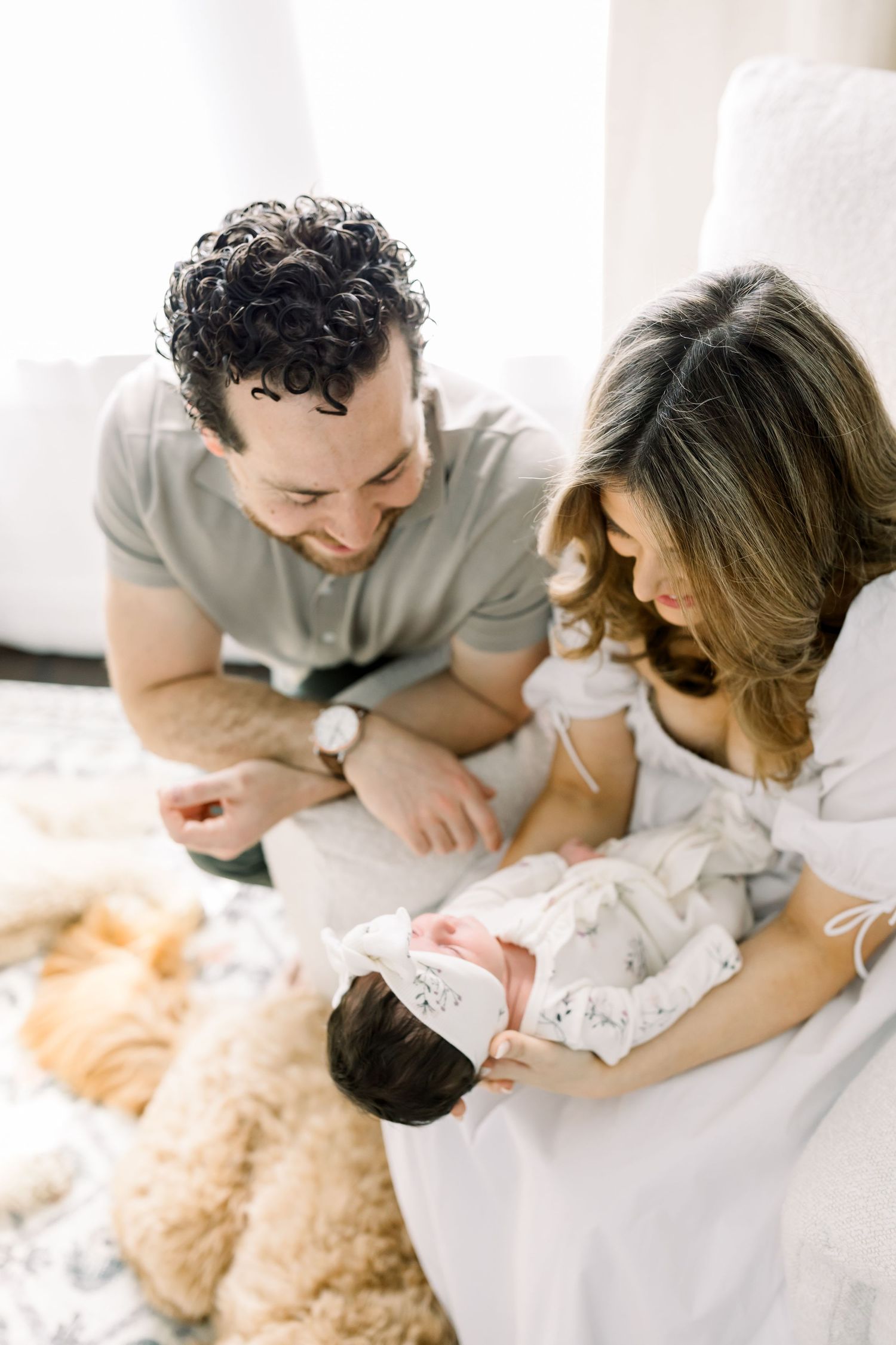 Family sitting together on a white couch with a goldendoodle dog nearby.