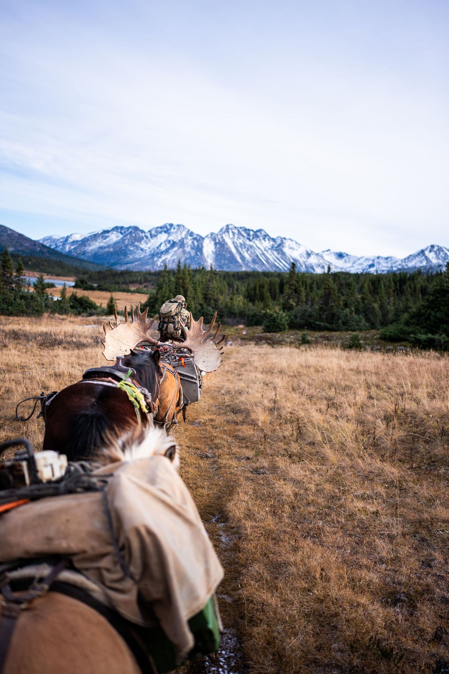 Horseback riders traverse a scenic mountain trail with snow-capped peaks in the distance.