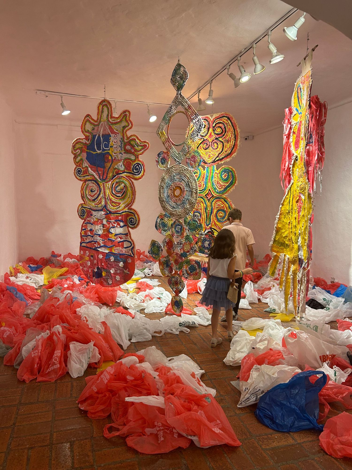 Art exhibition showing vibrant sculptural pieces with plastic bags scattered across terracotta flooring.