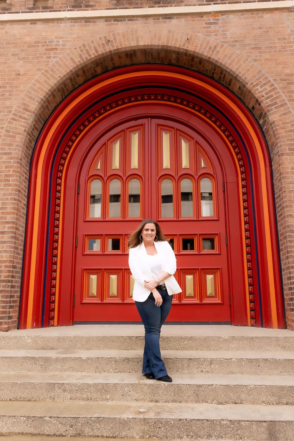 Professional fashion shoot featuring white blazer and dark denim against grand red doors.