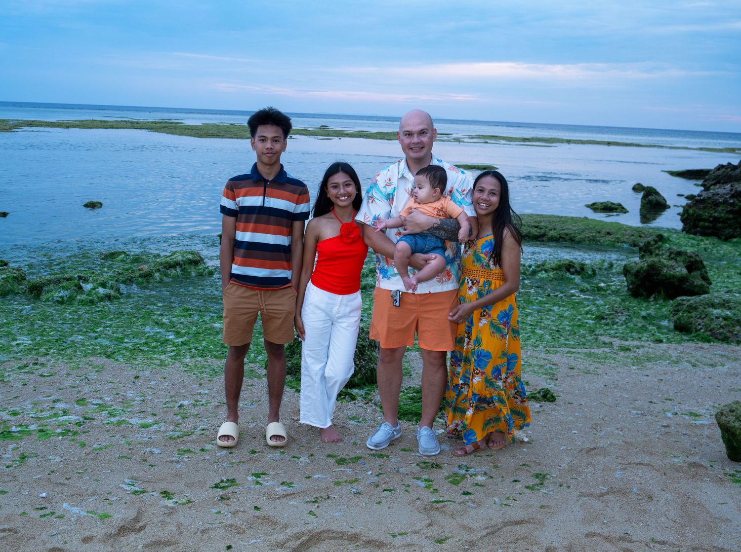 Group poses for casual photo by rocky coastline during sunset.
