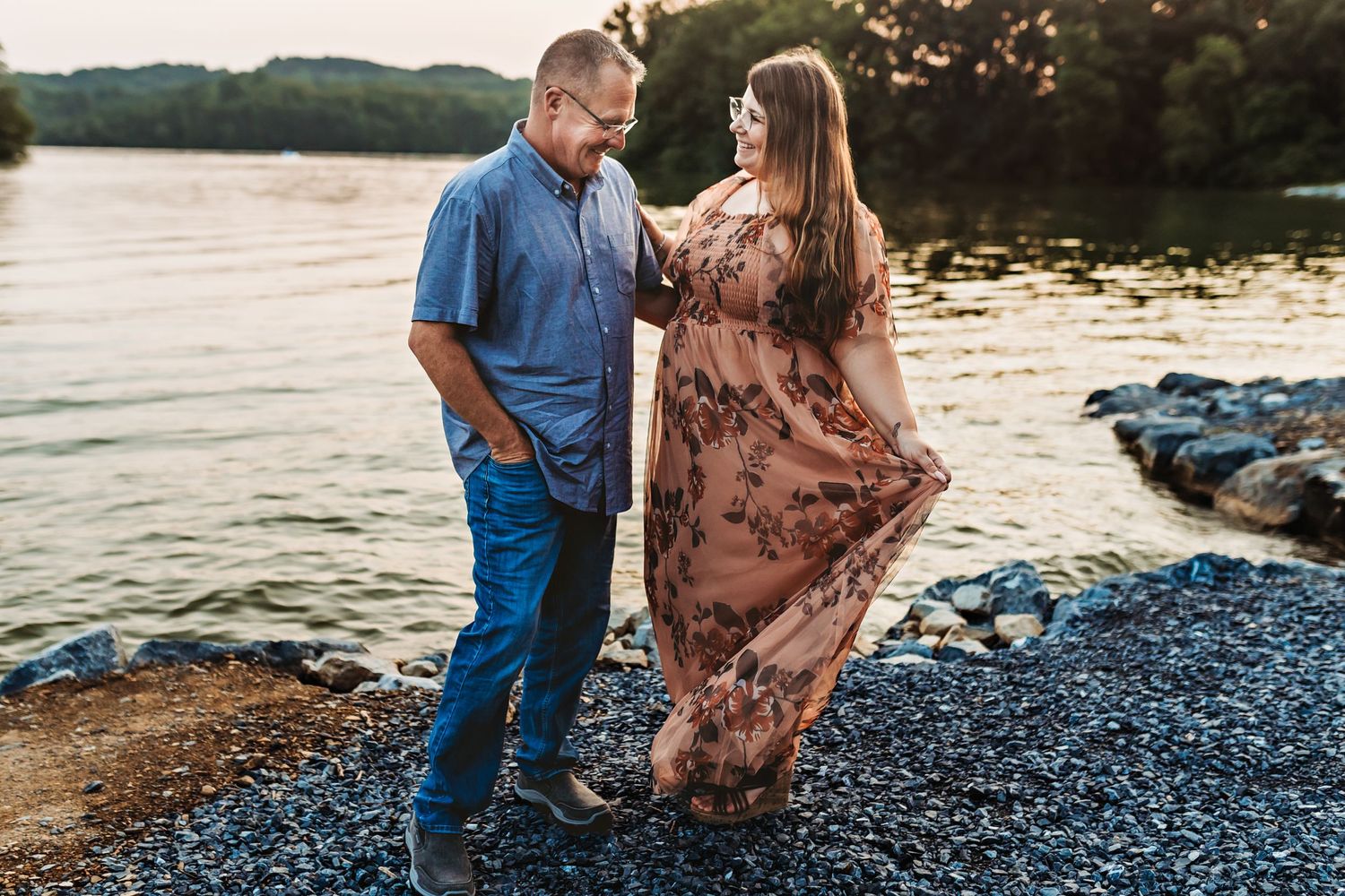 Woman dressed in a beautiful long flowy gown stands next to her husband wearing blue collared shirt and jeans
