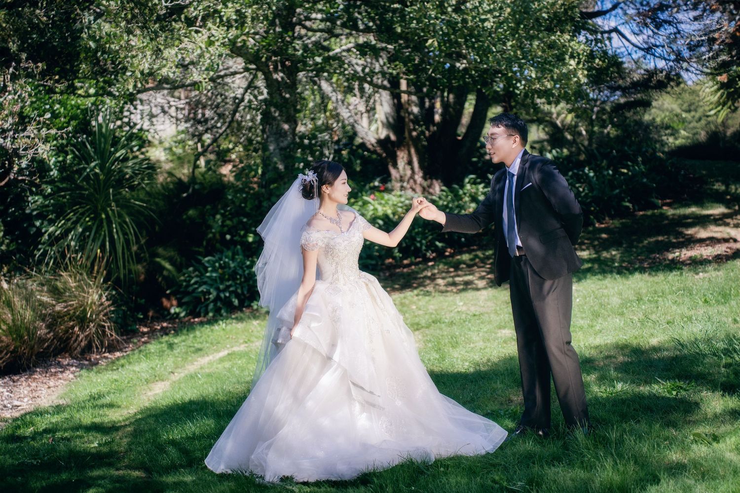 Engaged couple holding hands in a beautiful sunlit green garden for an Auckland outdoor pre-wedding photoshoot.