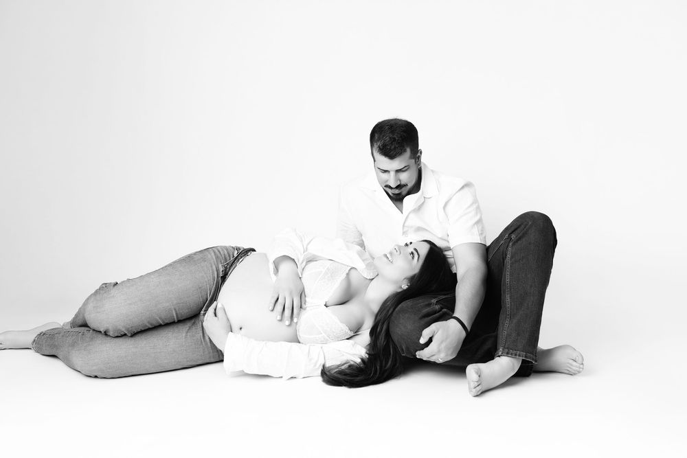 Black and white maternity photo of couple sitting on floor with pregnant woman resting head on mans lap.