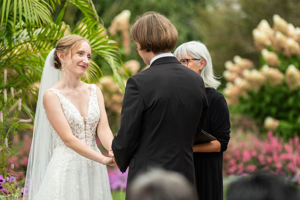 Garden wedding ceremony with couple and officiant surrounded by blooming flowers and greenery. Pittsburgh Wedding Photography, Videography