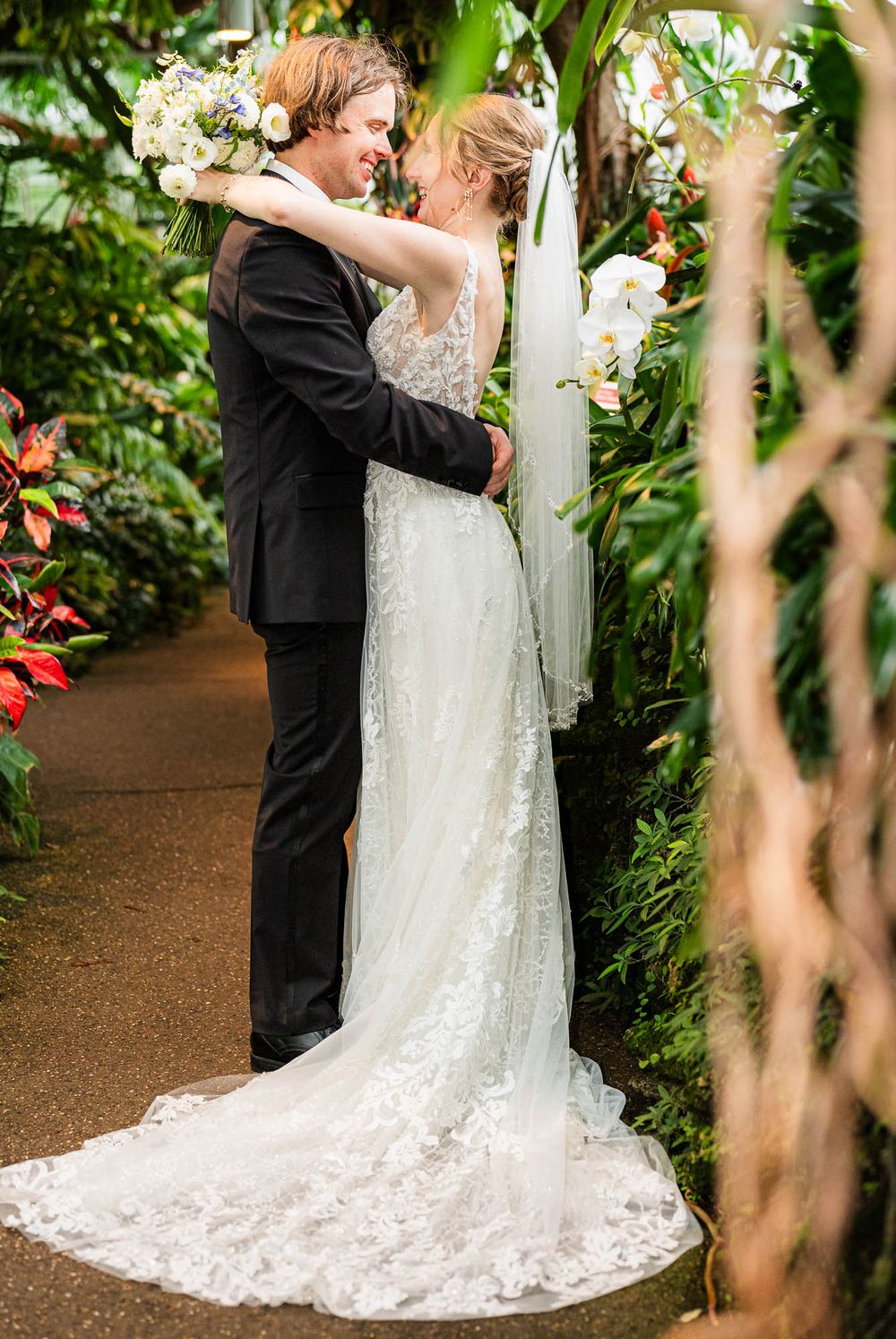 Romantic embrace between newlyweds on garden path with trailing lace wedding dress. Pittsburgh Wedding Photography, Videography
