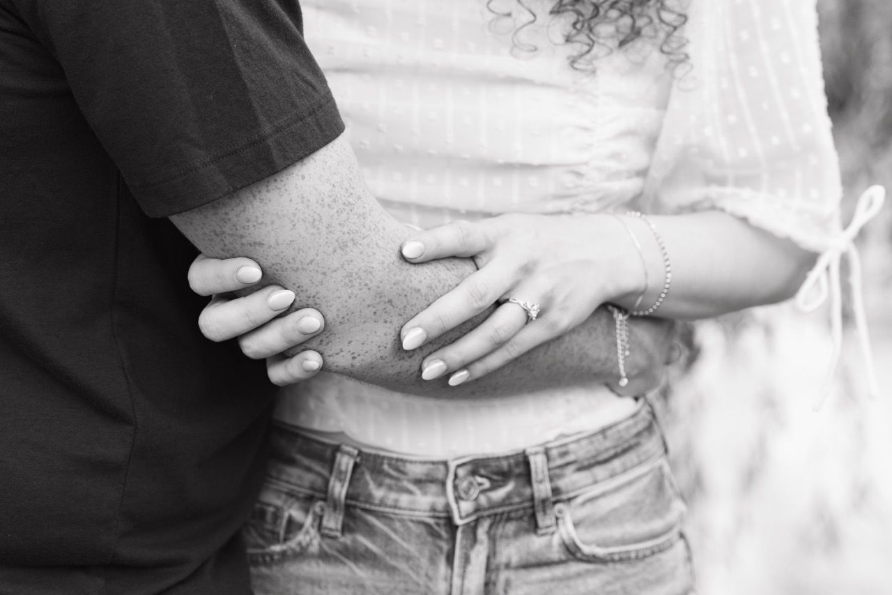 A black and white close-up photo shows hands gently embracing at the waist while wearing denim and casual clothing.